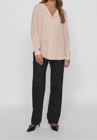Blusa rosa chiaro con scollatura a V e maniche lunghe, abbinata a pantaloni neri a gamba dritta e tacchi a punta neri.