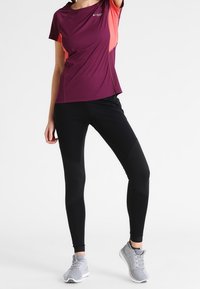 Kortärmad sporttop i mörklila och korall, kombinerad med svarta högmidjade leggings med meshpaneler. Grå löparskor fulländar outfiten.