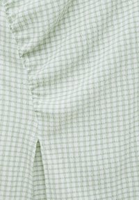 Grüner und weißer Gingham-Stoff mit einer strukturierten, gekräuselten Oberfläche. Besitzt einen seitlichen Schlitz und erscheint weich und leicht.
