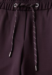 Pantalons de sport violet foncé avec une texture lisse, dotés d'une taille avec cordon de serrage et d'un accent argent�é, ainsi que de détails rayés blancs.