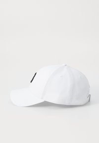 Fehér baseballsapka ívelt karimával, pamutból készült, elöl fekete logóval, a fejpánton szellőzőlyukakkal.