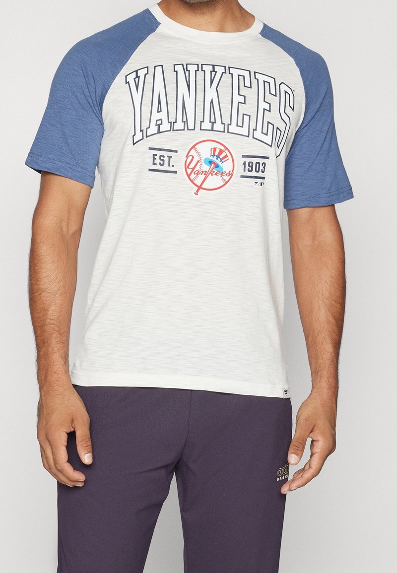 Valkoinen baseball-t-paita sinisillä raglan-hihoilla, jossa on "YANKEES"-teksti ja logo sekä vintage-beisball-kuva.