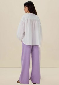 Witte oversized blouse met puffed mouwen, voorzien van een gathered achterkant. Gecombineerd met wijde lavendelkleurige broeken en zwarte sandalen.
