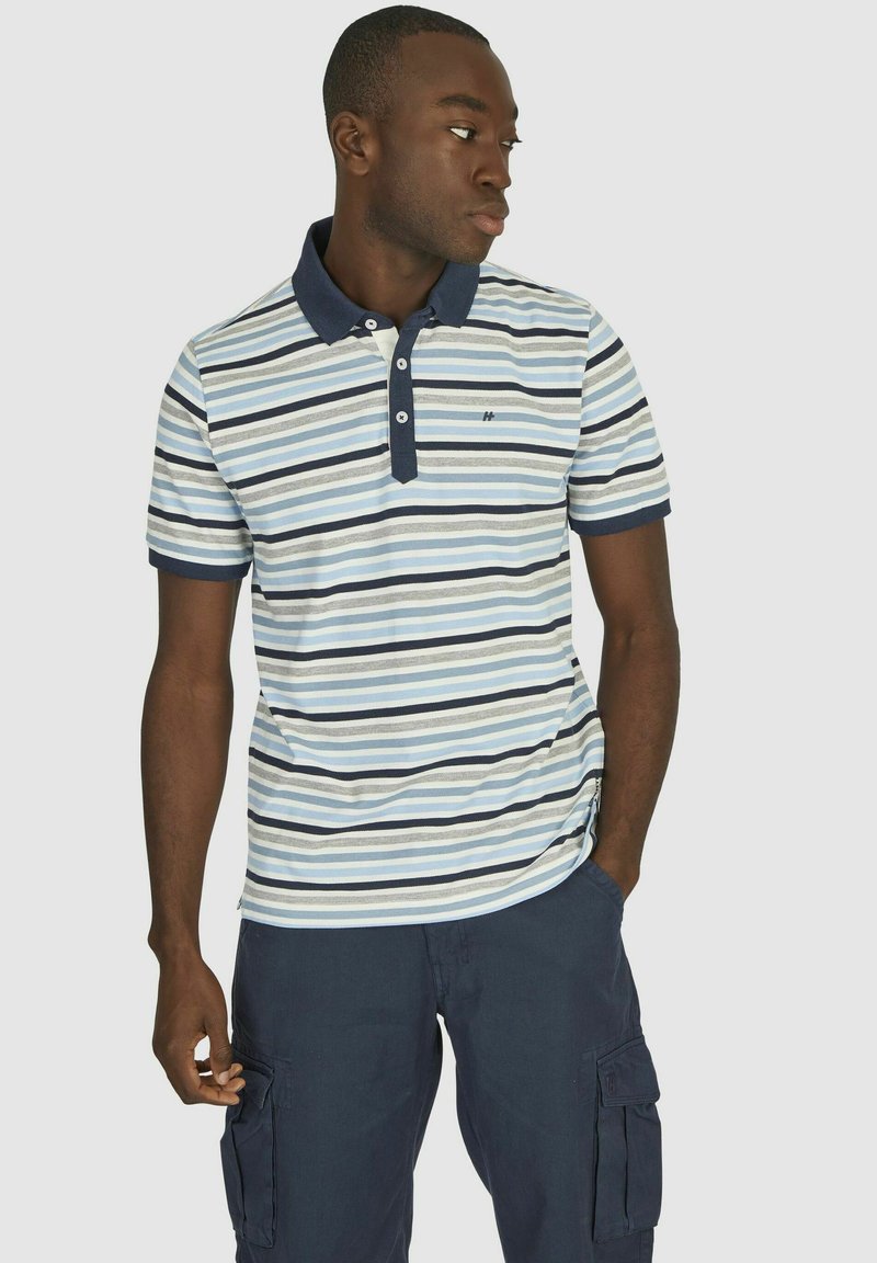 Gestreept polo shirt met afwisselend lichtblauw, marineblauw en witte tinten; heeft een marineblauwe kraag, een drieknopenlijst en korte mouwen.