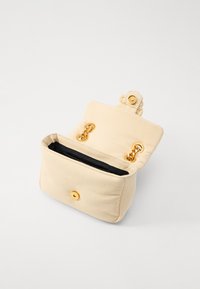 Beige stoffhåndveske med en myk tekstur, gullbeslag og sort innside. Har to gullkjede-låser og en gullsnap-lukking.