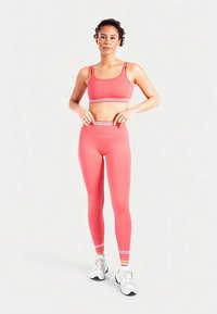 Roze atletisch cropped top en bijpassende leggings met witte strepen. Het materiaal lijkt rekbaar en aangesloten, ontworpen voor sportkleding.