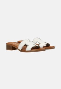 Sandalias deslizantes de piel blanca con diseño recortado y suela marrón, que cuentan con un tacón bajo y un detalle de costura en contraste.