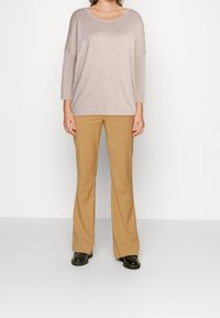 Maglione beige a maglia con scollo ampio e maniche a tre quarti, abbinato a pantaloni a palazzo color cammello e scarpe nere. Texture liscia nel complesso.