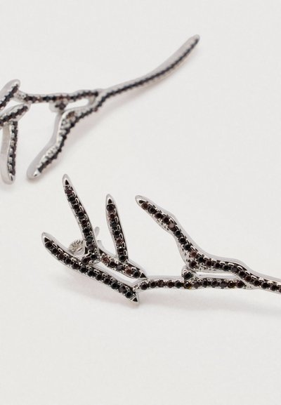 Grampas de cabelo em tom prateado, em forma de ramos, adornadas com gemas negras ao longo das bordas. Design fino e alongado com detalhes intrincados.