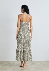 Maxi dress with thin straps, featuring a green and beige zebra stripe pattern, textured fabric, and a tiered hemline, view from the back.