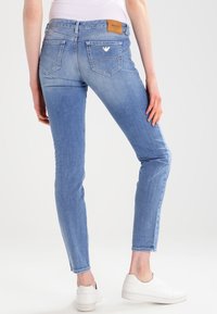 Jasnoniebieskie szczupłe jeansy o gładkiej fakturze, z dwoma tylnymi kieszeniami i skórzaną metką na pasku w talii. W połączeniu z białymi wsuwanymi butami.