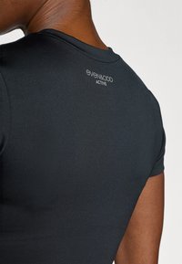 Sort aktivtøjstop med tætsiddende design, korte ærmer og glat tekstur. Har et logo i en kontrastfarve på bagsiden ved halsudskæringen.