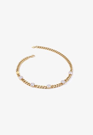 Złoty naszyjnik łańcuszkowy z dużymi, przezroczystymi kamieniami osadzonymi pomiędzy ogniwami, z bezpiecznym zapięciem i małym dekoracyjnym akcentem w kształcie trójkąta.