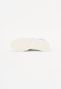 Semelle de chaussure en caoutchouc blanc avec un motif de semelle en chevron. Accents bleus visibles sur la partie supérieure, bout plat et légèrement arrondi.