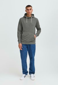 Hoodie gris avec une poche frontale, un cordon de serrage réglable et des poignets côtelés, associé à un jean en denim bleu et des baskets blanches.