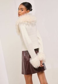 Bílý texturovaný svetr s nadýchaným krémovým límcem a manžetami, spárovaný s bordó sukní z umělé krokodýlí kůže. Celkový vzhled obsahuje jedinečné akcenty.