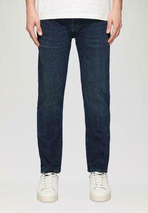 Dark blue denim jeans with a straight cut, featuring subtle fading and whiskering, paired with white sneakers.