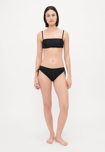 Bikini negro con un top bandeau de tirantes finos y braguitas laterales ajustables con lazo. Textura suave, diseño minimalista y silueta estilizada.
