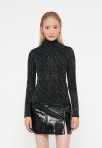Melnā turtlenecks kreklā ar sudraba viļņu rakstiem, pieguļošs dizains, garas rokas, apvienots ar spīdīgu melnu mini svārku ar sānu iegriezumu.