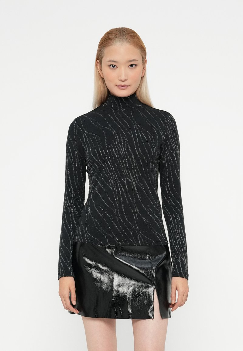 Melnā turtlenecks kreklā ar sudraba viļņu rakstiem, pieguļošs dizains, garas rokas, apvienots ar spīdīgu melnu mini svārku ar sānu iegriezumu.