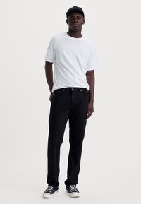 Zwarte denim jeans, witte crewneck t-shirt en een donkere pet. Casual stijl, aansluitende snit, met sneakers met witte zolen en veters.