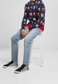 Pull bleu avec des accents rouges représentant le Père Noël et des flocons de neige, associé à un jean bleu clair et des baskets montantes à carreaux noirs.