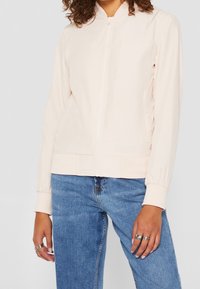 Ljusrosa zip-up bomberjacka med rund krage, elastiska ärmslut och ett något texturerat tyg. Matchad med blå denimjeans.