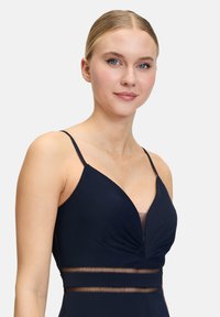 Robe bleu marine à fines bretelles, dotée d'un décolleté en V profond et d'un buste plissé. Un panneau transparent à la taille ajoute du détail.