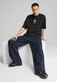 Black oversized t-shirt with a graphic design, paired with loose dark blue denim jeans. Footwear features a multi-colored design with red and purple accents.