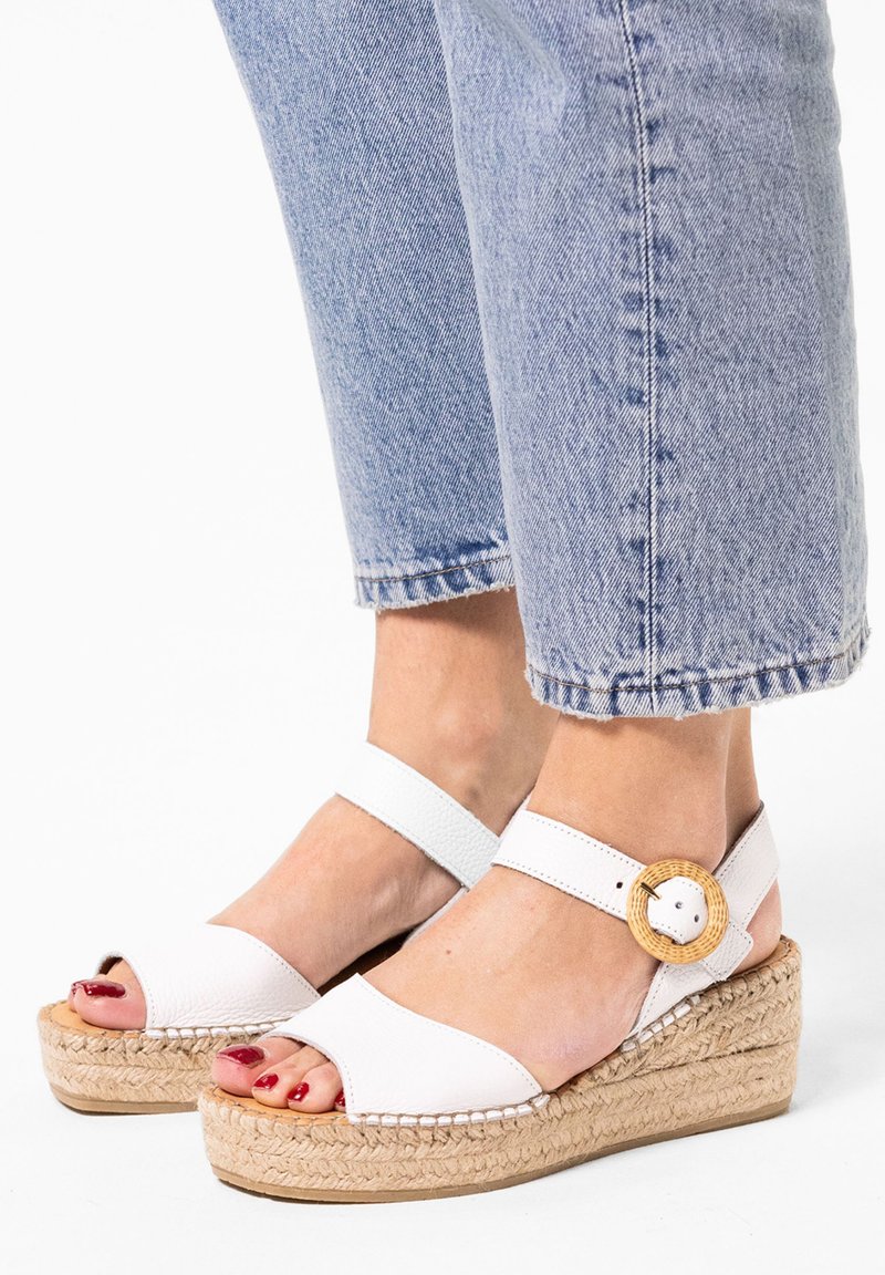 Witte leren wedge-sandalen met een gevlochten touwzool, voorzien van een verstelbare strap en een grote ronde bamboe-accent aan de zijkant.
