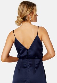 Abito di satin blu navy con profondo scollo a V sulla schiena, spalline sottili regolabili e zip centrale. Presenta una vita aderente con pieghe sottili.