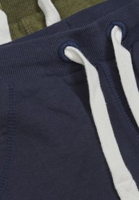 Marineblå joggingbukser med hvide fleece snore, med ribbet talje og tekstureret stof. Andet par i olivengrøn synligt ovenfor.