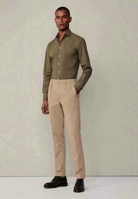 Olivgrön knapp-up skjorta med slim fit, kombinerad med ljusbeiga byxor. Bruna skor avslutar looken. Slät tyg, skräddarsydd design.