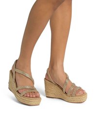 Sandales compensées beiges avec des semelles en jute tressé, ornées de multiples bandes horizontales comportant de petits strass pour des accents décoratifs.