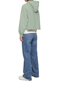 Hellgrüner, kürzer geschnittener Kapuzenpullover mit gerippter Struktur, kombiniert mit lockeren blauen Jeans und weißen Turnschuhen.