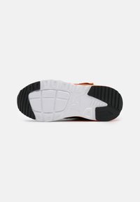 Black and white sneaker sole with an orange accent. Tread pattern includes rectangular and circular indentations for traction. Flexible design.