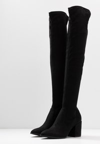 Bottes noires au-dessus du genou en daim doux, avec un design épuré, un bout pointu et un large talon bloc pour la stabilité.