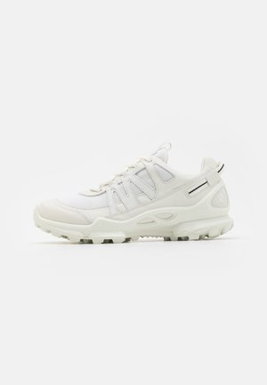 White athletic shoe featuring a mesh upper, molded accents, textured sole, and multi-directional tread. Lacing system with pull tab at heel.