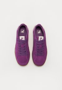Lilla semsket sneakers med rund tå, flate lisser og gummisåle. Har kontrasterende hvit logo og såle i gummifarge.