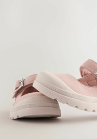 Sandalias de ante rosa con punta cerrada, correa ajustable con un hebilla plateada y una suela blanca con surcos texturizados.