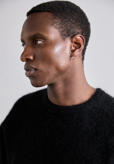 Suéter negro texturizado con un cuello redondo, llevado por un modelo masculino con el cabello corto y muy corto, y un pequeño aro en la oreja.