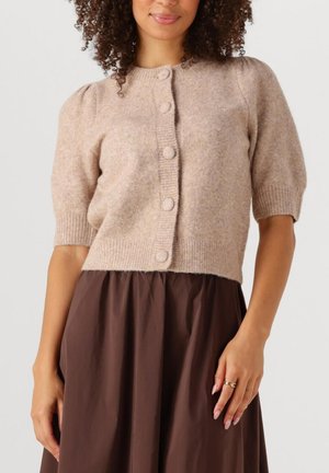 Short-sleeved, beige cardigan with textured fabric, round buttons down the front, and ribbed cuffs. Worn over a dark brown skirt.