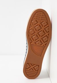 Semelle de sneaker Converse All Star, en caoutchouc gomme avec un motif en losange, accents latéraux noirs et coutures blanches le long du bord.