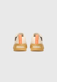 Zapatillas beige con una pestaña trasera naranja, suela de goma texturizada y marca blanca en el talón. Material superior suave con acentos en contraste.