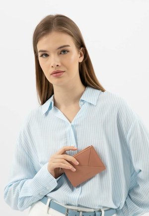Light blue striped shirt with a relaxed fit, holding a tan leather cardholder featuring a geometric design and a zippered pocket.