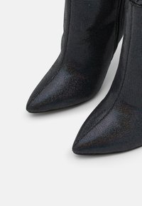 Botas pretas de bico fino com um material em malha texturizada e refletiva, e um fecho de correr elegante ao longo do lado.