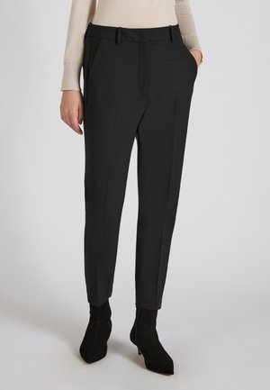 Zwarte op maat gemaakte broeken met een gladde textuur, voorzien van zijzakken en een slim fit. Gecombineerd met zwarte puntige enkellaarsjes.