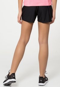 Svarta atletiska shorts med en avslappnad passform, med en mjuk textur och rundad nederkant. Bärs med svarta träningsskor och en rosa topp.