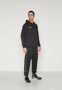 Hanorac negru cu grafică "KING", asortat cu pantaloni jogging negri cu dungi laterale modelate. Purtați cu adidași negri sport.