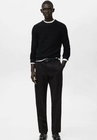 Maglione nero con trama e scollo tondo bianco, abbinato a pantaloni neri sartoriali e scarpe nere. Design semplice e moderno.